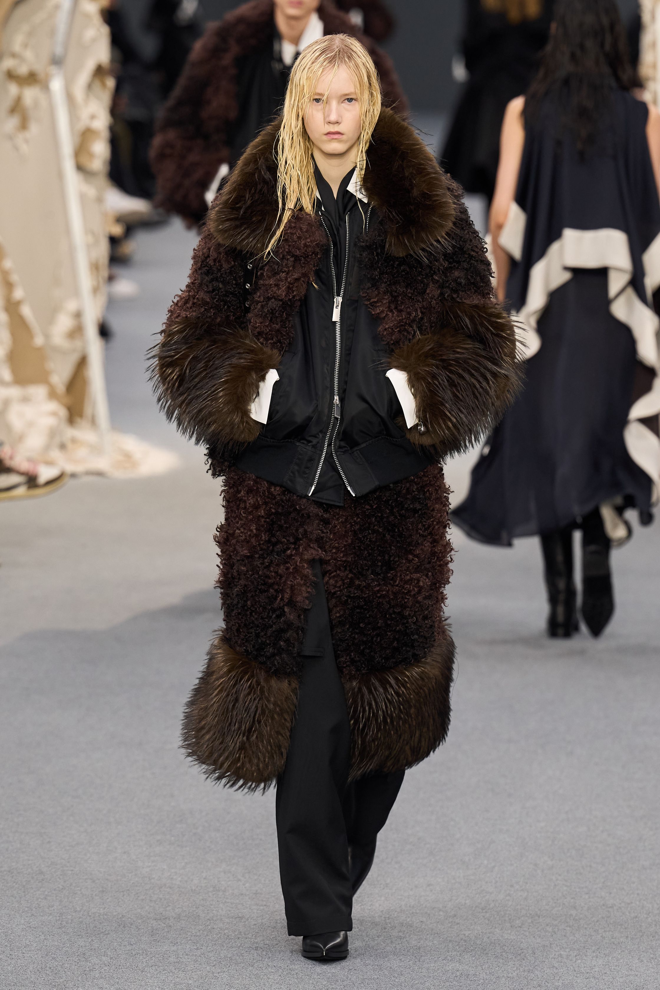 Sacai 2026秋冬再次展示其无可复制的“混合美学”。正装、牛仔、皮草与制服元素被高度结构化地拼接，形成既熟悉又陌生的服装形态。性别边界被进一步模糊，层叠结构制造流动节奏，使行走本身成为设计的一部分。系列在秩序与混乱之间找到平衡，是Sacai 对当代复杂生活状态的持续回应-顽石频道趋势研究